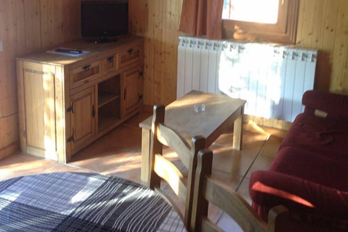 A room with wooden walls, a television on a wooden cabinet, a window with curtains, a table, and a red chair.