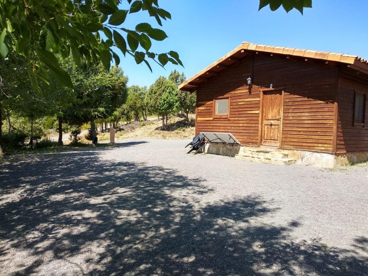 A wooden cabin with a gravel driveway, a covered outdoor seating area, and a small window.