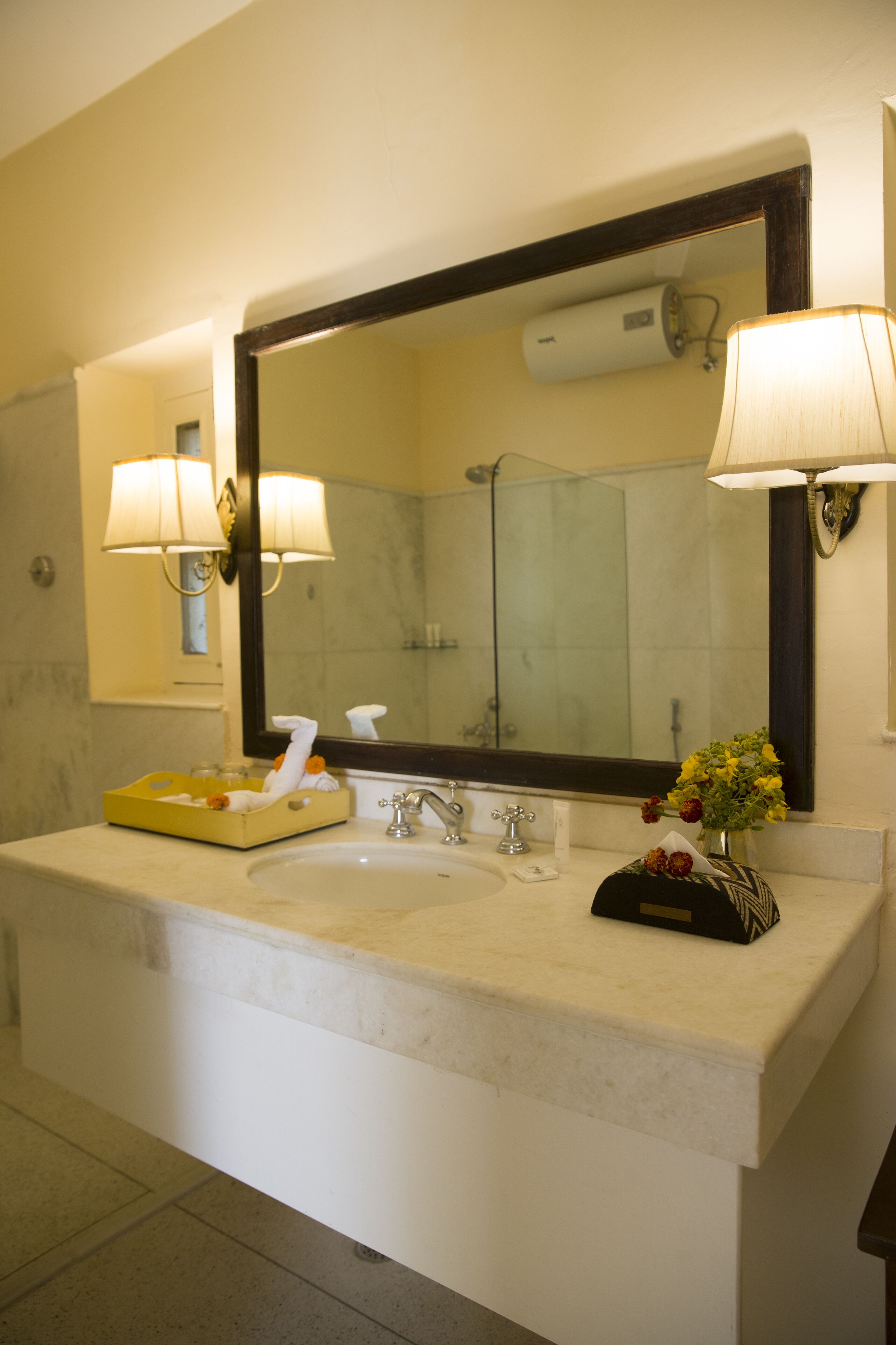 A bathroom with a large mirror, two wall-mounted lamps, a sink, and a towel rack.