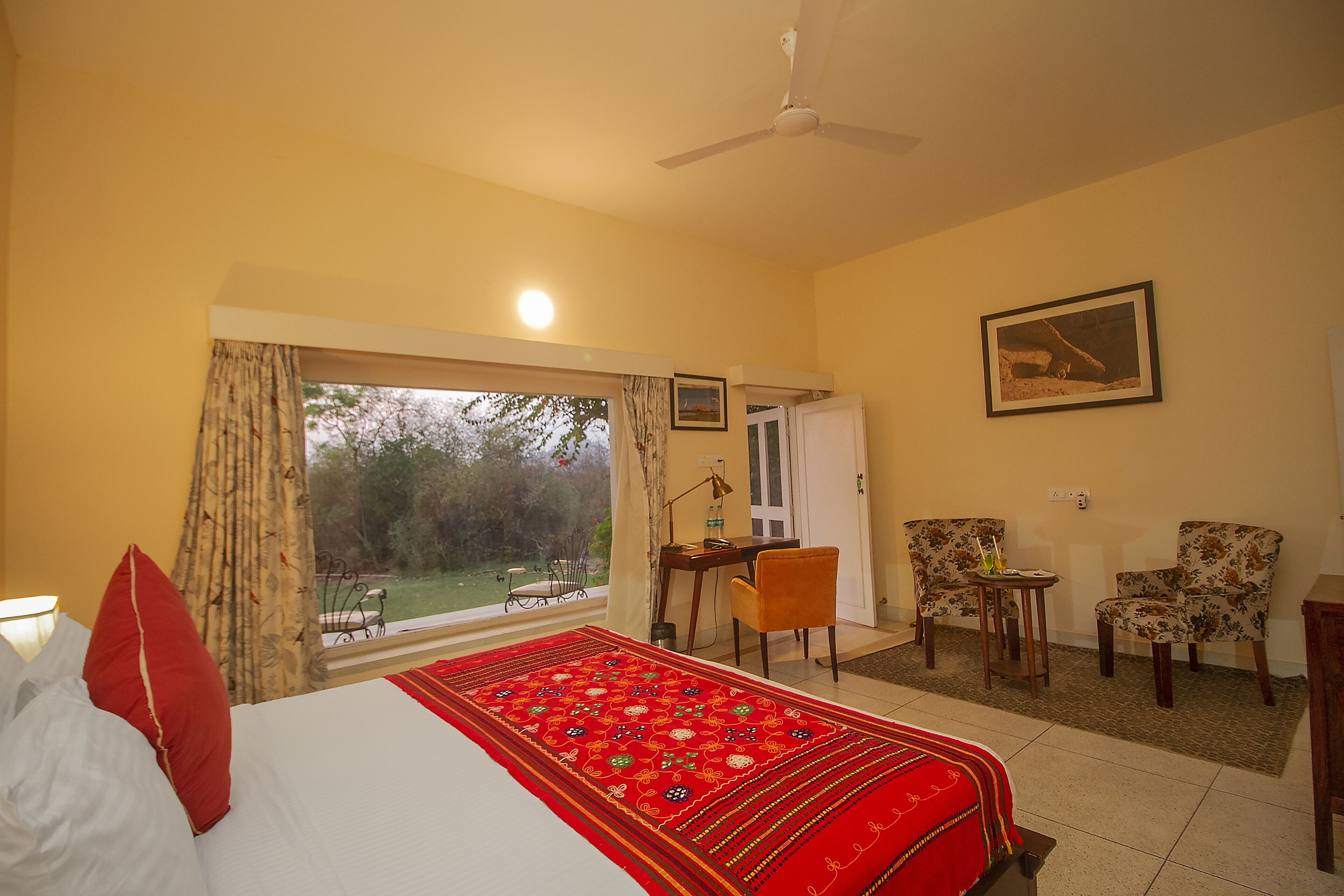 A hotel room with a bed, a desk, two chairs, a small table, and a large window.