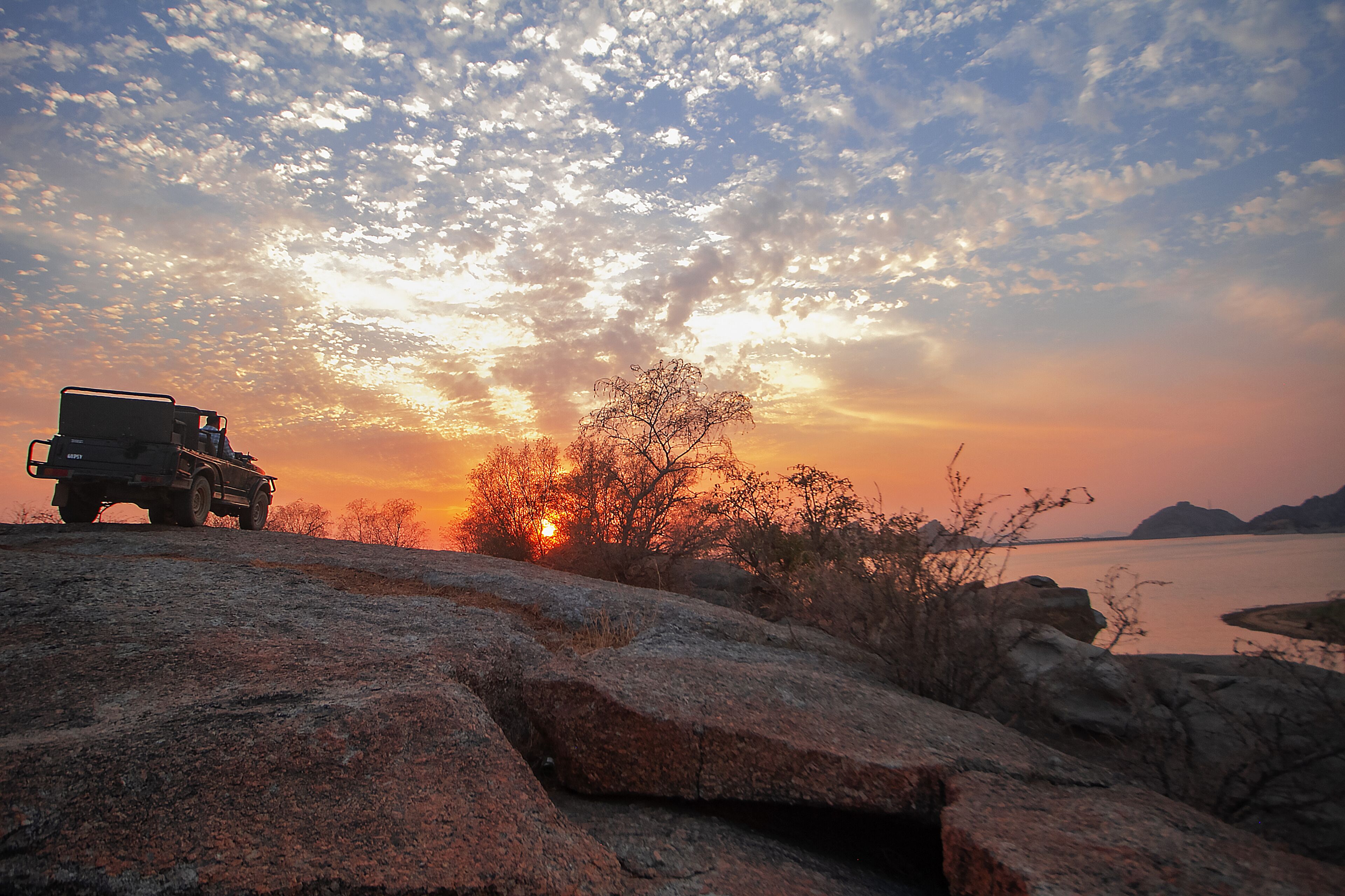 A jeep on a rocky terrain with a sunset in the background.