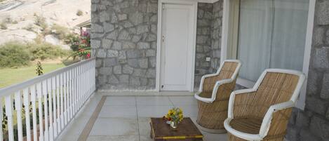 A balcony with stone walls, a white door, two wicker chairs, and a small table with flowers.