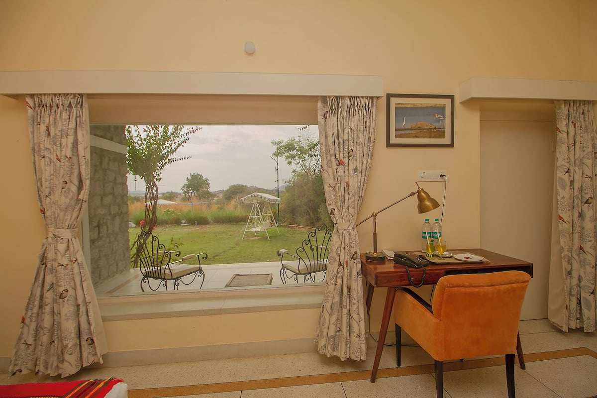 Ein Zimmer mit Schreibtisch, Stuhl und Blick auf einen Garten durch ein Fenster.