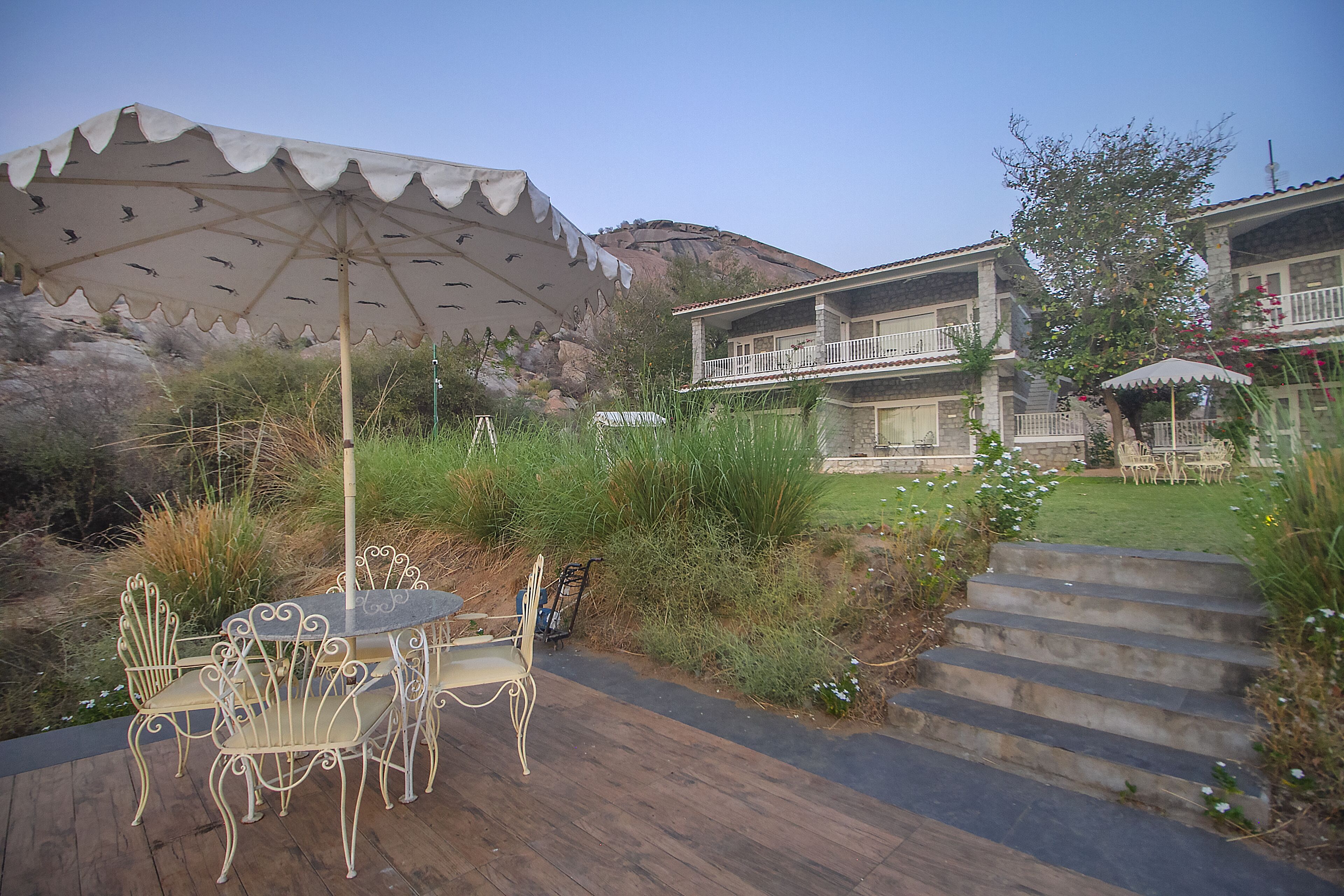 Une terrasse avec une table et des chaises, un grand parasol et un bâtiment doté d’un balcon.