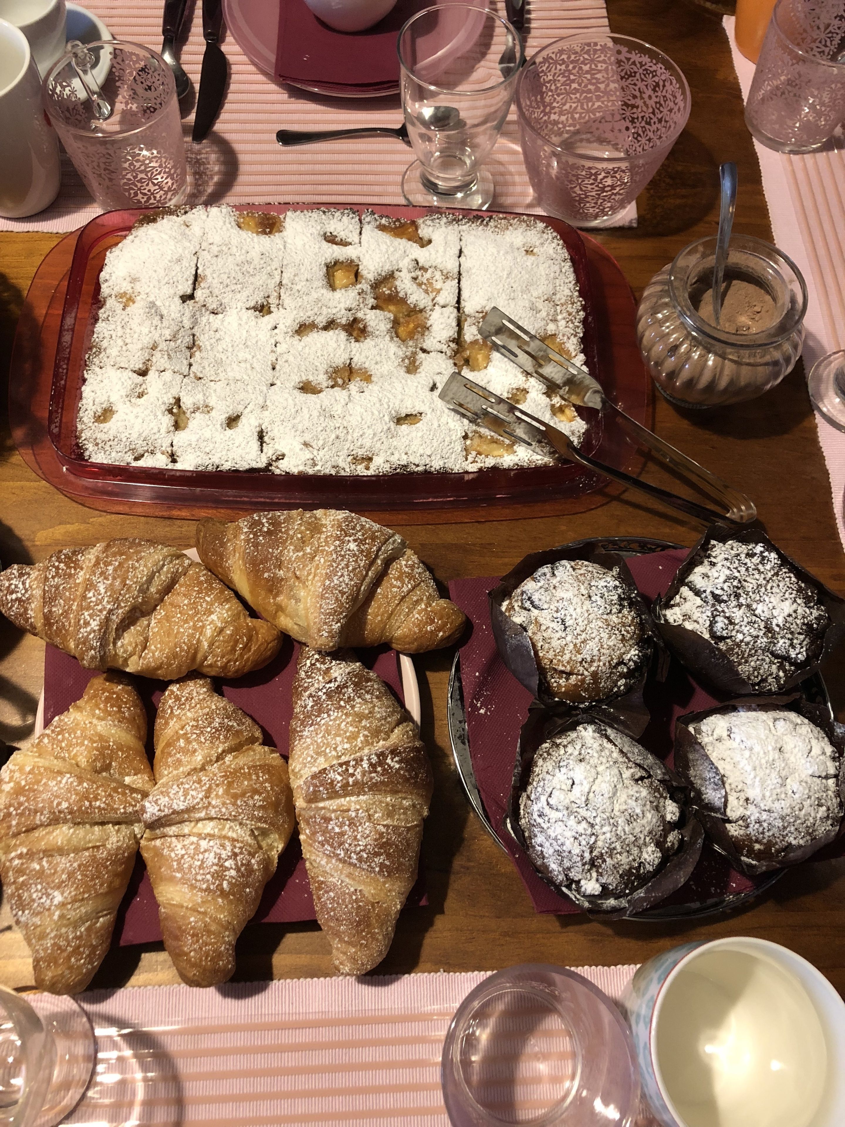 A dessert tray with a lattice-topped cake, a selection of croissants, and powdered pastries on a table with a striped tablecloth.