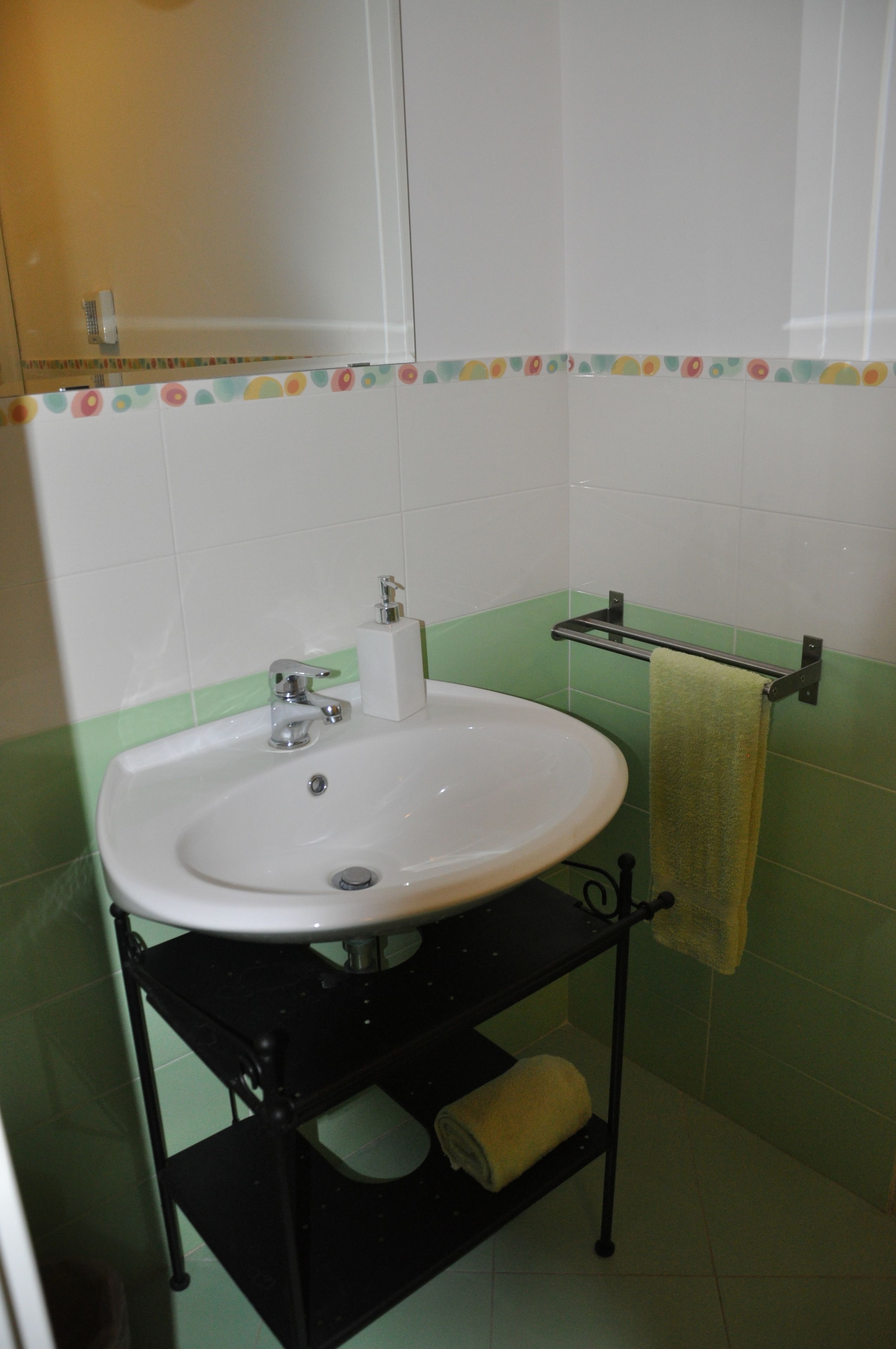 Ein Badezimmer mit weißem Waschbecken, Wänden aus grün-weißen Fliesen, einem Handtuchhalter und einem Toilettenpapierhalter.