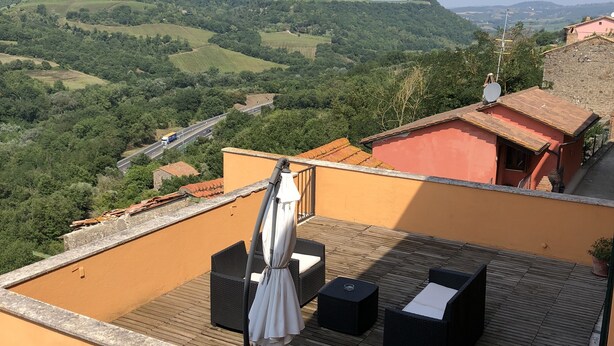 A rooftop terrace with outdoor furniture, a view of the countryside, and a building with a red roof. - Dimora Paolina (Baschi)