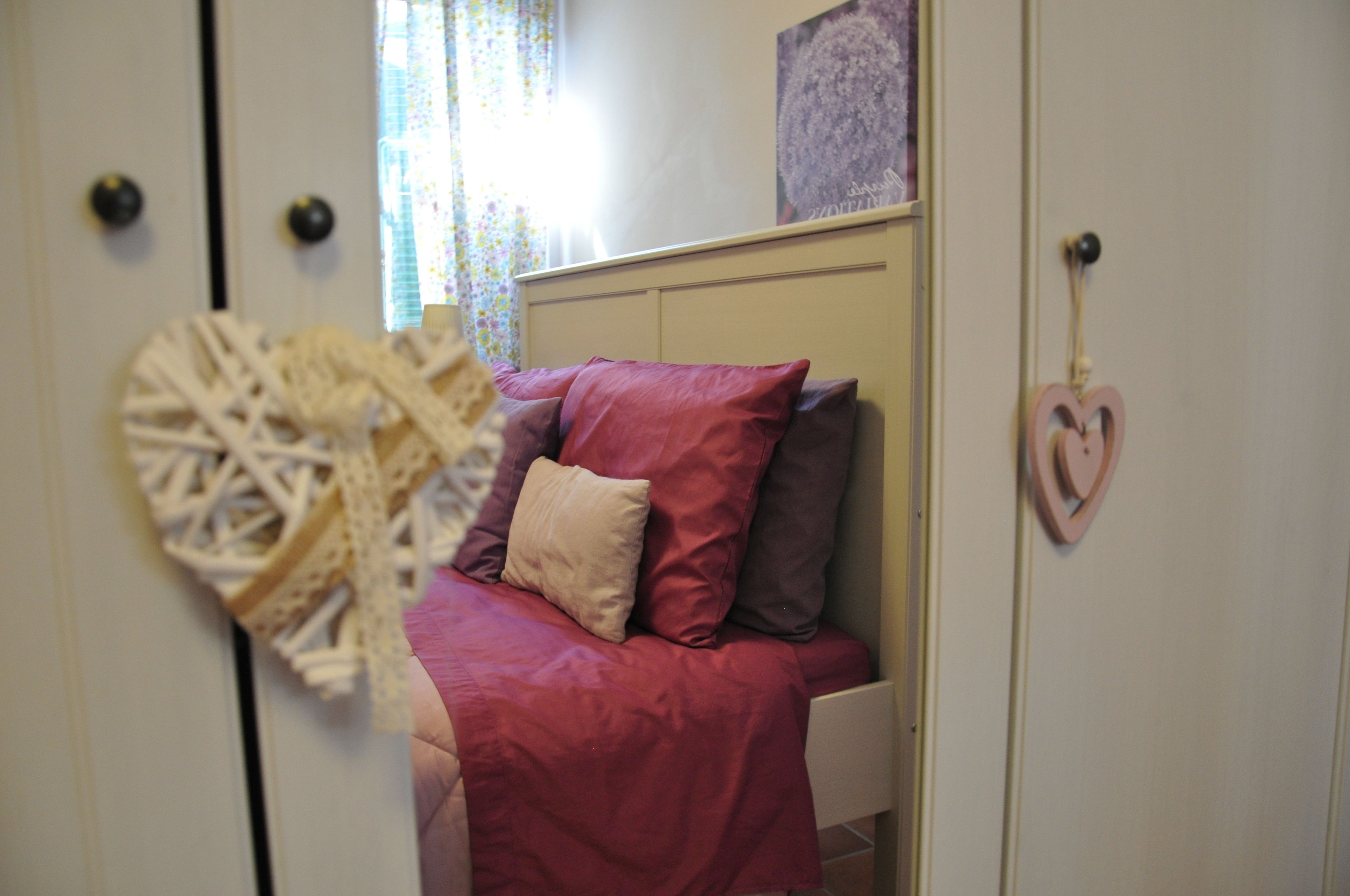 Une chambre à coucher avec un lit, des oreillers, une décoration en forme de cœur et un objet en dentelle accroché au mur.