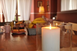 A candle in a glass holder on a wooden table in a room with a sofa and curtains. - Dimora Paolina (Baschi)