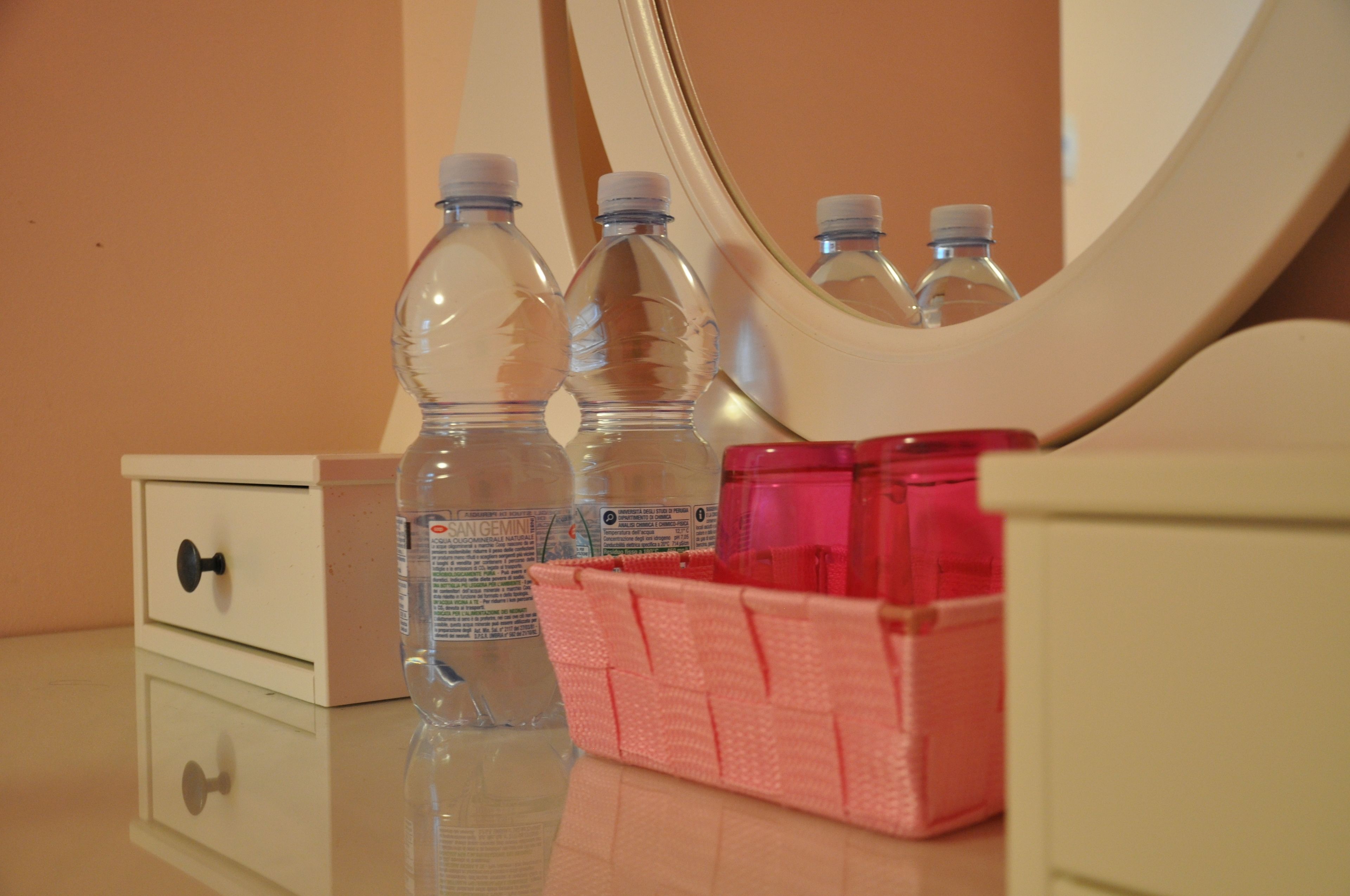 A bathroom vanity with a mirror, a white drawer, and a pink basket.