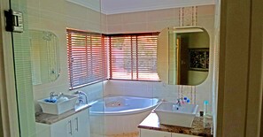 Un baño con bañera, dos lavamanos y una ventana con persianas.