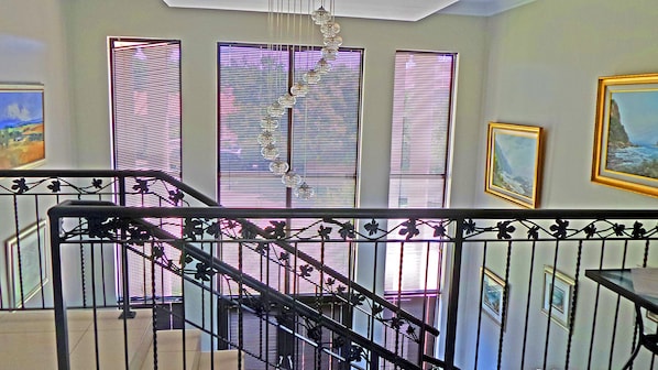 A staircase with a metal railing, leading to a landing with three windows with blinds.