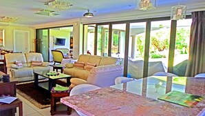 A spacious living room with a large window, a television, and a dining area with a table and chairs. - Jeanette's Villa at Westlake (Hartbeespoort)