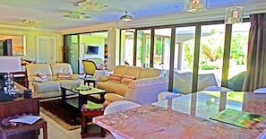 A spacious living room with a large window, a television, and a dining area with a table and chairs.