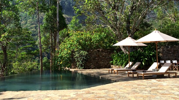 A pool area with lounge chairs and umbrellas, surrounded by stone walls and lush greenery. - The Planters House (Koslanda)