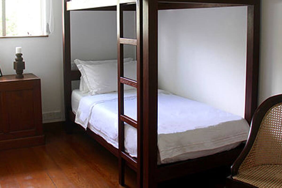 Ein Stockbett mit weißer Bettwäsche, eine Holzkommode und ein Korbstuhl.