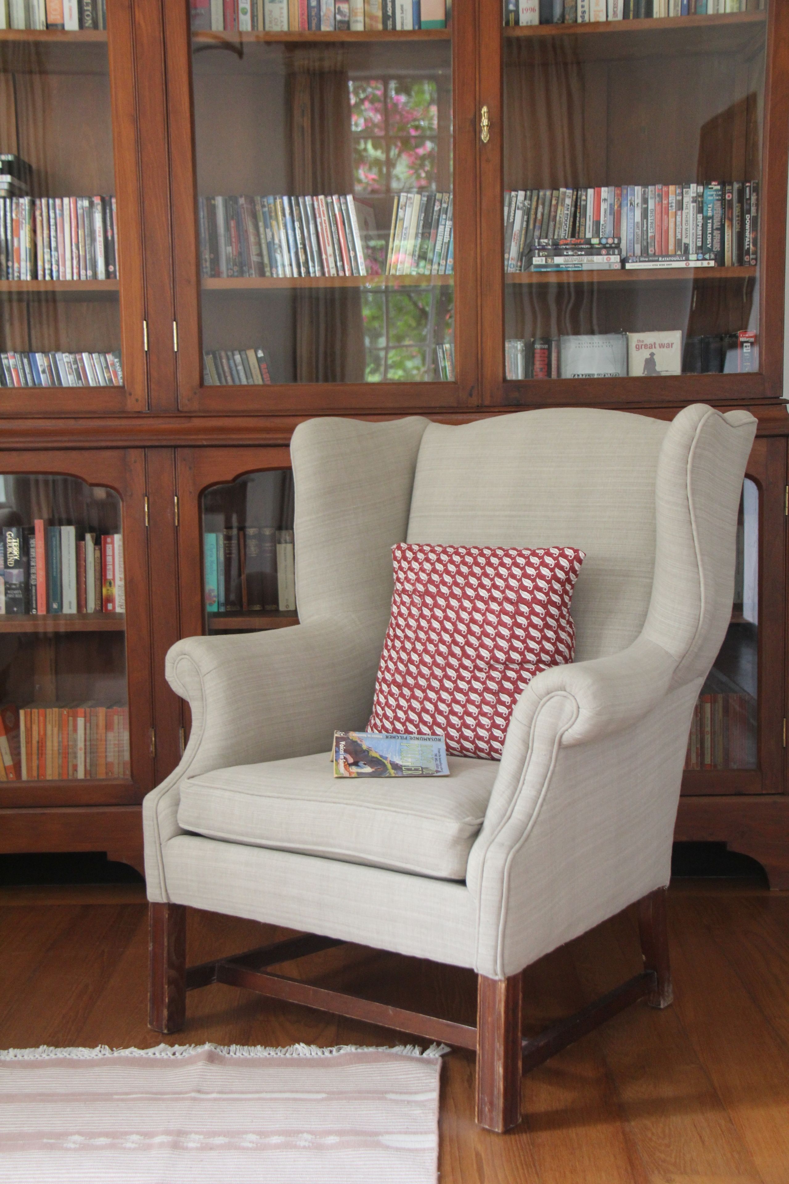 Un salon avec un fauteuil beige, un coussin à motifs et une bibliothèque remplie de livres et de DVD.