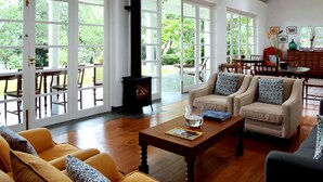 A spacious living room with a wooden floor, large windows, a fireplace, and comfortable seating. - The Planters House (Koslanda)