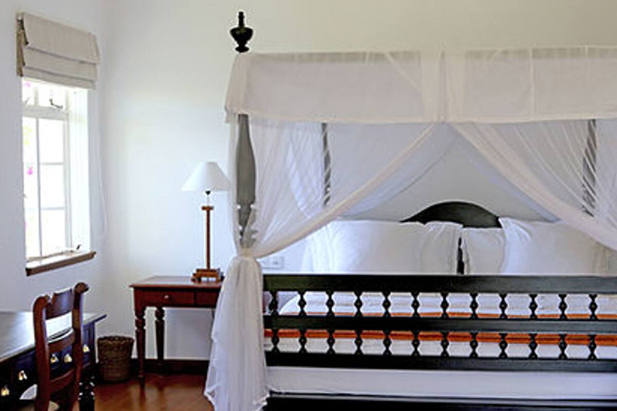 Ein Schlafzimmer mit einem Himmelbett, einem Nachttisch, einer Lampe und einem Sessel.