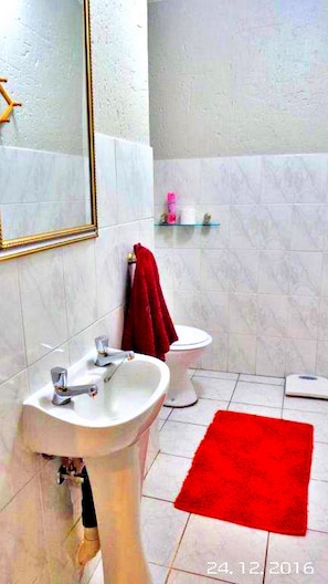 A bathroom with a sink, toilet, and a red rug. - Key West Condo Apartment (Hartbeespoort)
