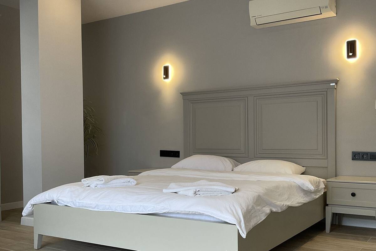 Un dormitorio con cama, mesitas de noche, un equipo de aire acondicionado e iluminación en la pared.