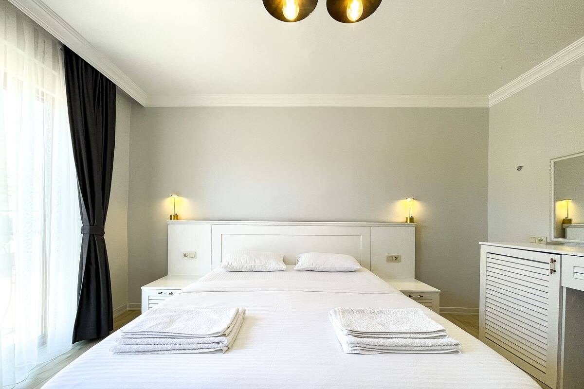 Una habitación de hotel con una cama grande, dos lámparas de noche, un aparador y un espejo.