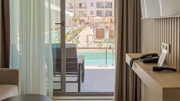 Quarto de hotel com varanda, uma mesa de trabalho com telefone e vista para a área da piscina.