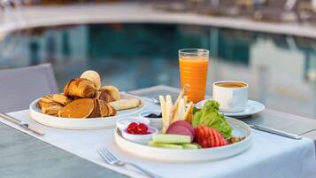 Desayuno con cruasanes, fruta y jugo junto a una piscina.