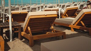 Un área de descanso frente a la playa, con hileras de sillones de madera y sombrillas color beige.