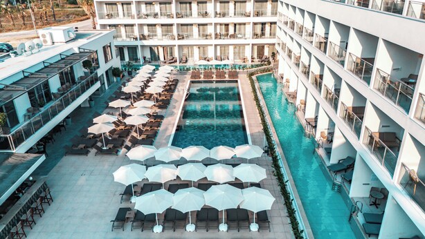 Un hotel con piscina central rodeada de tumbonas y sombrillas, varios balcones y un diseño arquitectónico moderno.