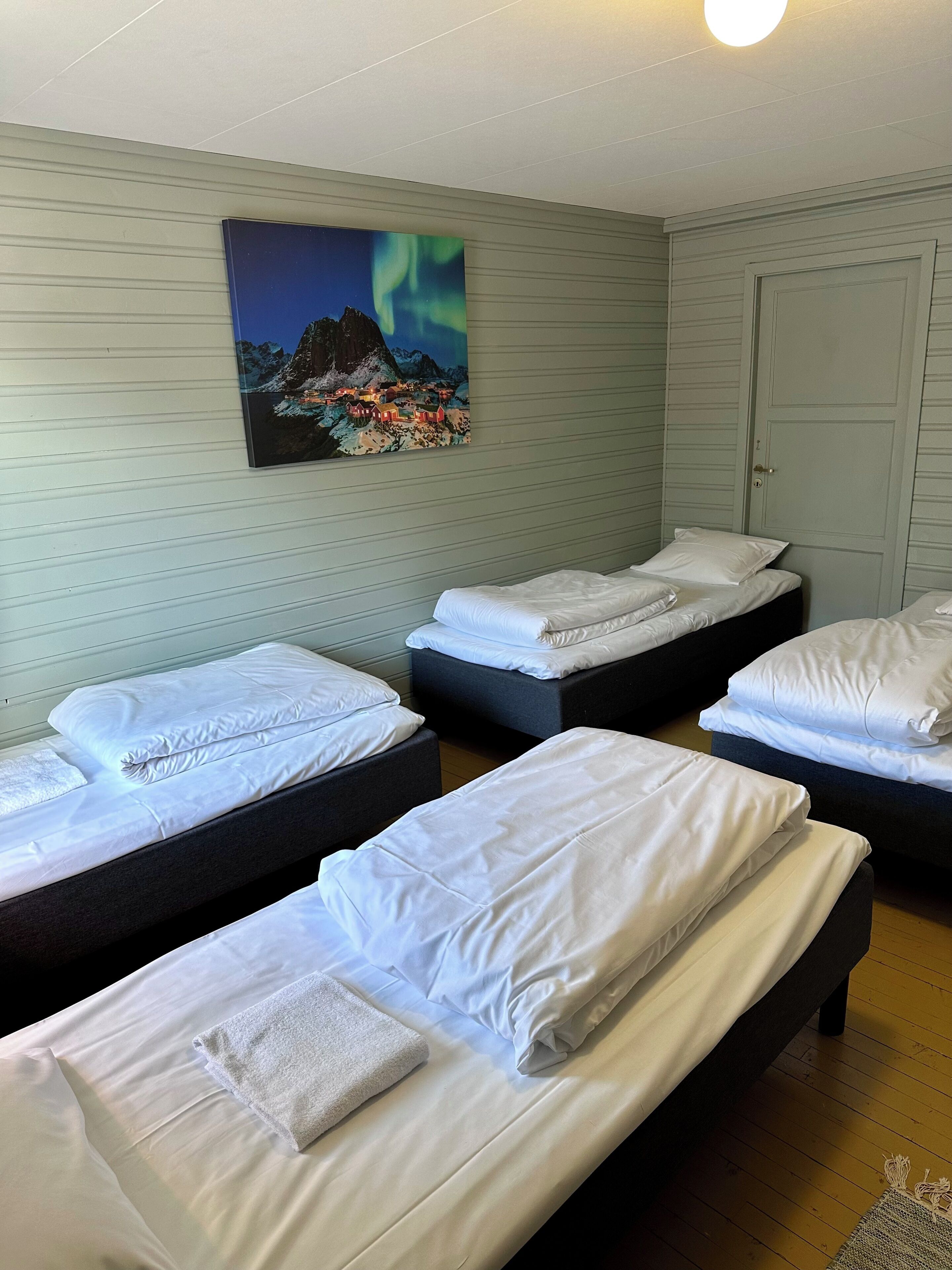 Ein Hotelzimmer mit vier Einzelbetten, einem Gemälde einer Berglandschaft und einer geschlossenen Tür.