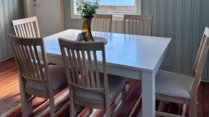 A dining area with a table, chairs, a vase, and a view of mountains and water through a window. - Lydersen Rorbuer (Flakstad)