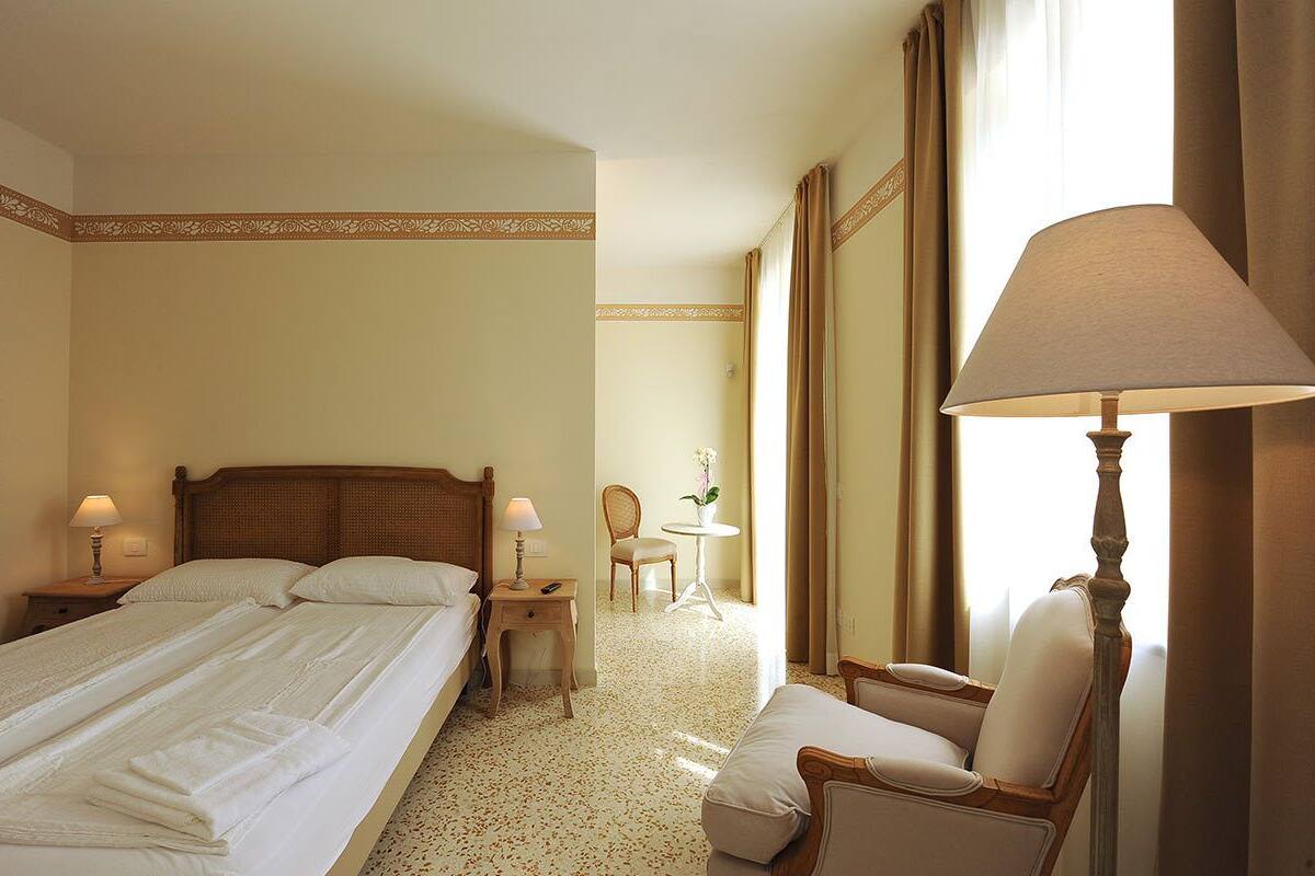 Una habitación de hotel con una cama grande, una silla, una mesita con lámpara y un espejo.
