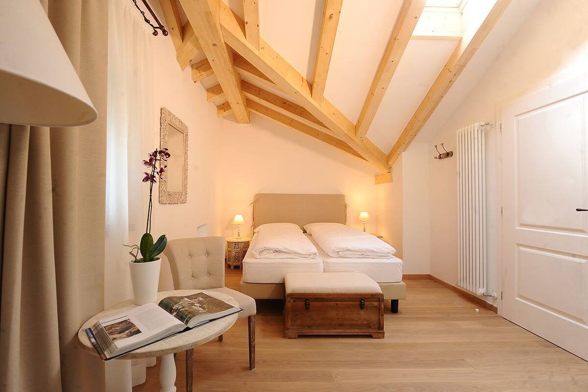 Un dormitorio con cama, mesitas de noche, una silla, una pequeña mesa con un libro y una planta en maceta.