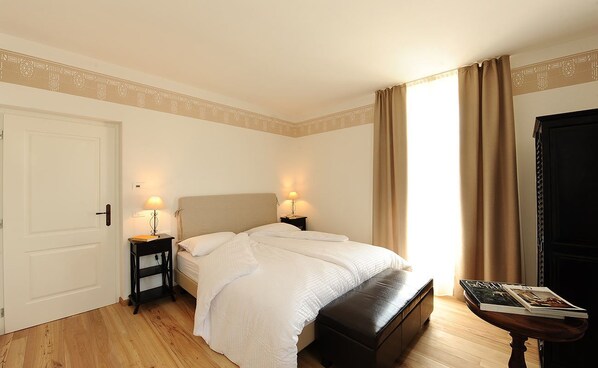 A bedroom with a bed, bedside tables, a bench, and a door. - La Villa degli Orti (Borgo Valsugana)