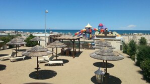 Una località balneare con ombrelloni di paglia, lettini da spiaggia e uno scivolo d'acqua.