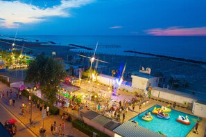A beachside area with a swimming pool, beach umbrellas, and a Ferris wheel. - Hotel Sara (Rimini)