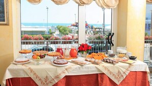 Un tavolo da buffet con diversi pasticcini, frutta e bevande, con vista panoramica sull'oceano.
