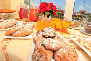 Un buffet de petit-déjeuner avec des viennoiseries, une carafe de jus de fruits et un vase rempli de fleurs.