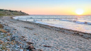 A beach with a pier extending into the water, surrounded by pebbles and seaweed. - Nice home in Knebel with house sea view (Knebel)
