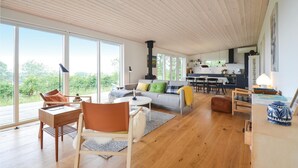 A spacious living area with a large window, a sofa, a dining table, and a kitchen in the background. - Nice home in Knebel with house sea view (Knebel)