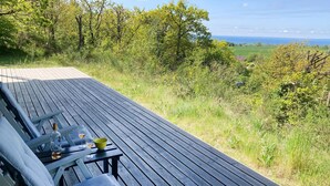 A wooden deck with a table and chairs, overlooking a grassy landscape with trees and a distant view of the sea. - Nice home in Knebel with house sea view (Knebel)