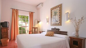 Quarto com cama, televisão, luminária, quadro emoldurado e vaso com plantas.