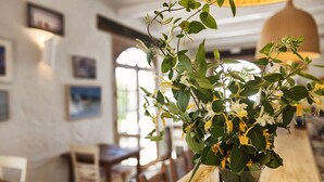 Interior de restaurante com um balcão de madeira, cadeiras e um vaso de flores no balcão.