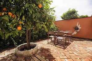 A patio with a table and chairs, surrounded by a brick floor and a tree with oranges. - Hotel Madreselva (Barbate)
