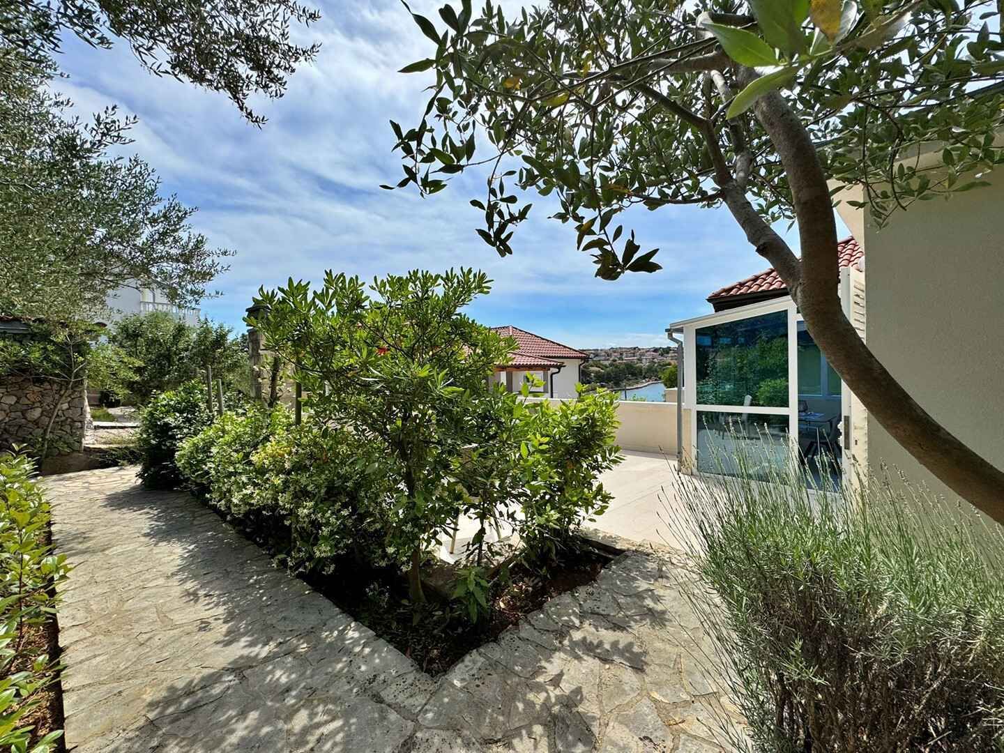 Un sentiero in pietra conduce a una casa con tetto in tegole rosse, immersa nel verde e sotto un cielo sereno.