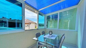 A sunlit room with a glass table and chairs, large windows, and a view of houses. - Holiday apartment with sea view 20 m from the coast (Šilo)