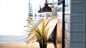 Une plante en pot, posée sur une chaise en osier, près d’un lit, avec une lampe suspendue au-dessus.