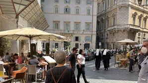 Une rue pavée bordée de cafés avec des terrasses, des bâtiments historiques et un ciel d’un bleu éclatant.