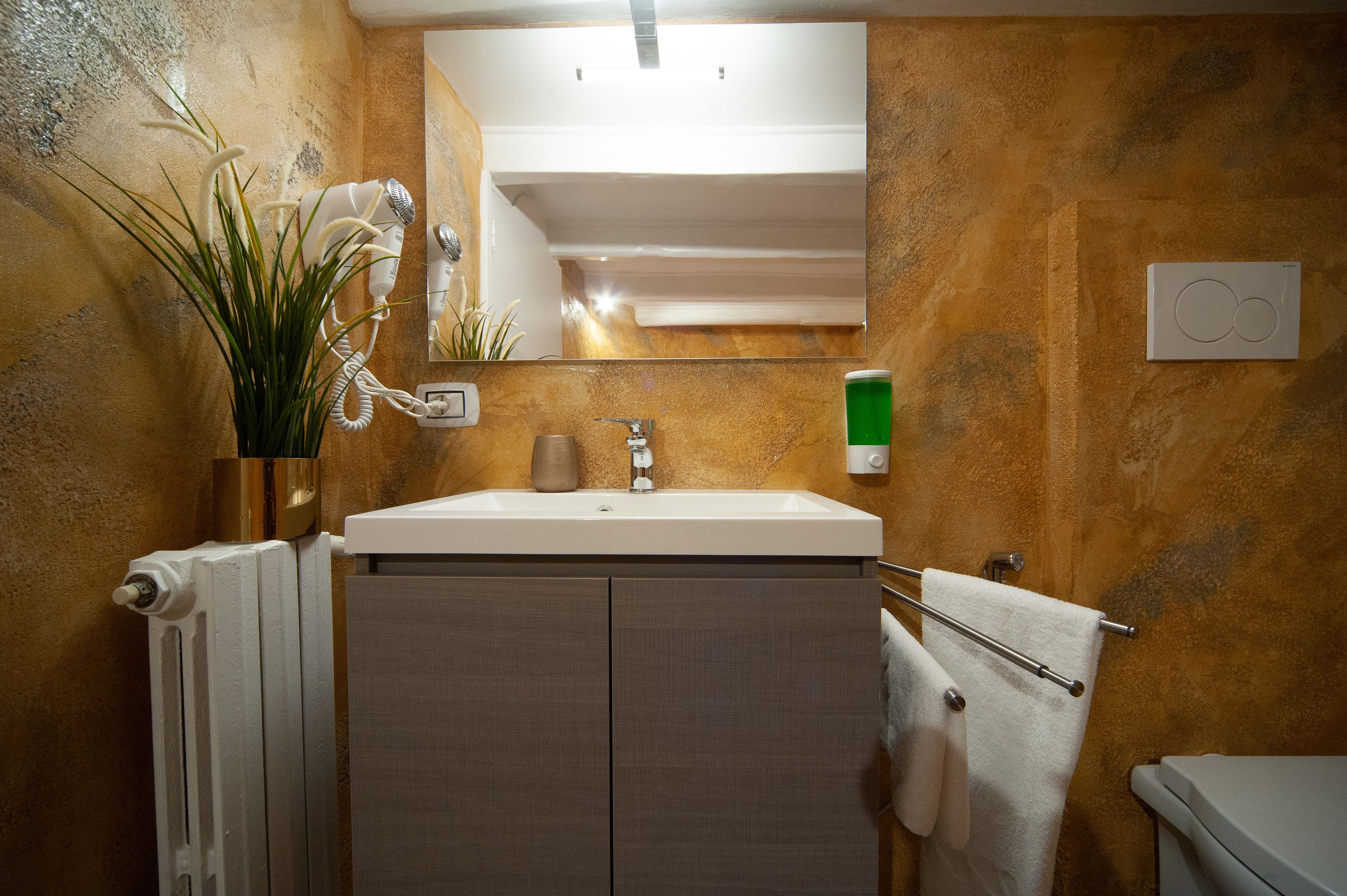 Un baño con un lavamanos blanco, un espejo encima, un perchero y un radiador.